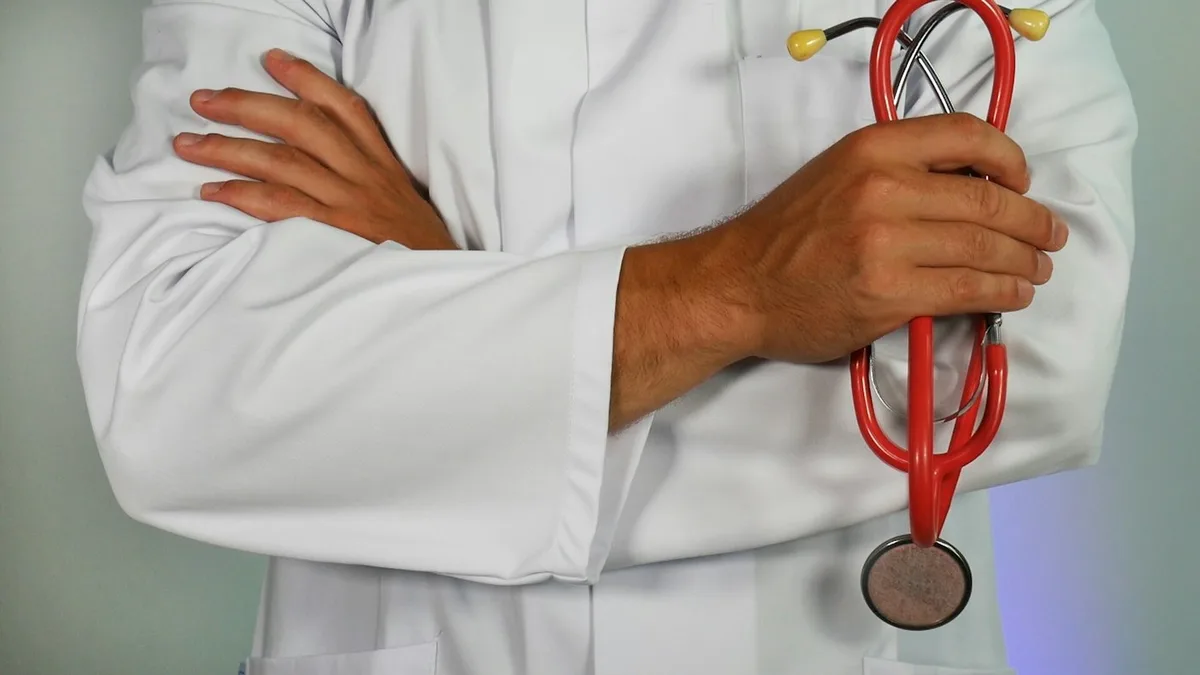 Médico de braços cruzados segurando um estetoscópio vermelho